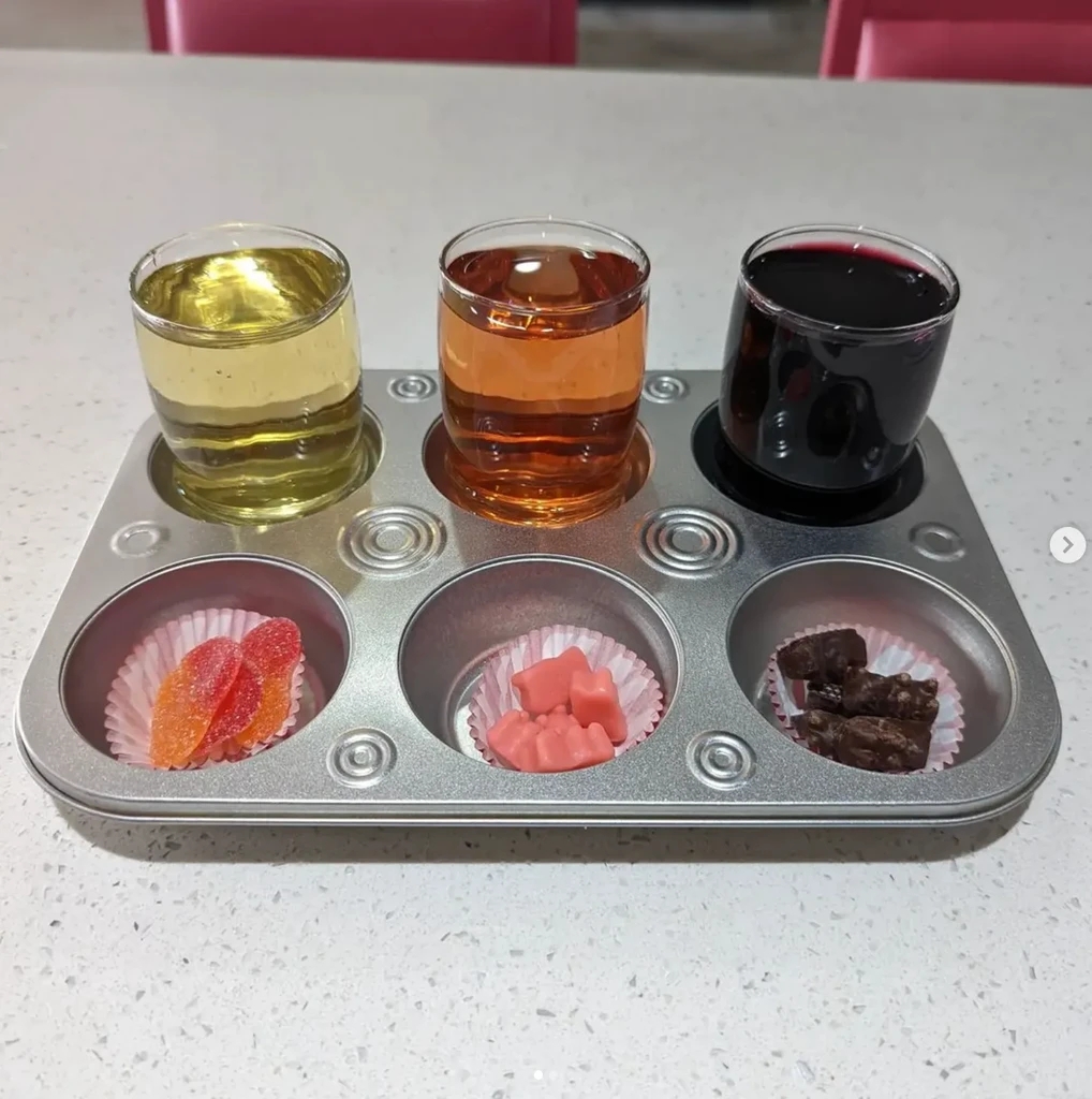 Metal muffin tin serving colored liquids and assorted candies.