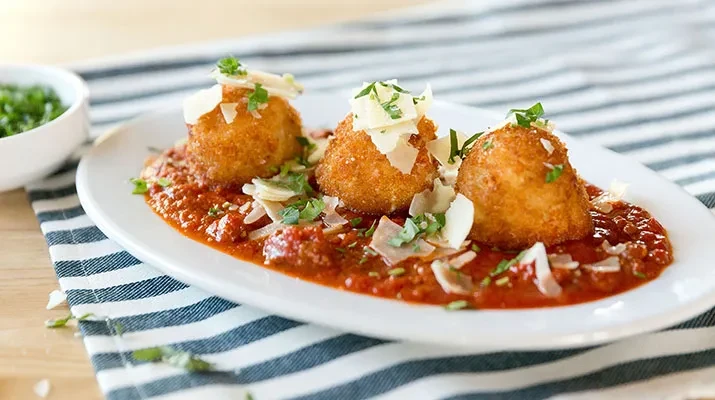 Three fried spheres on tomato sauce topped with Parmesan and herbs.
