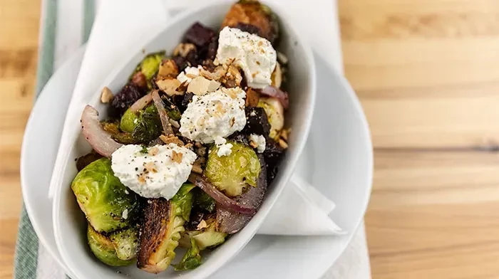Close-up of roasted Brussels sprouts, root vegetables, creamy cheese, and nuts.