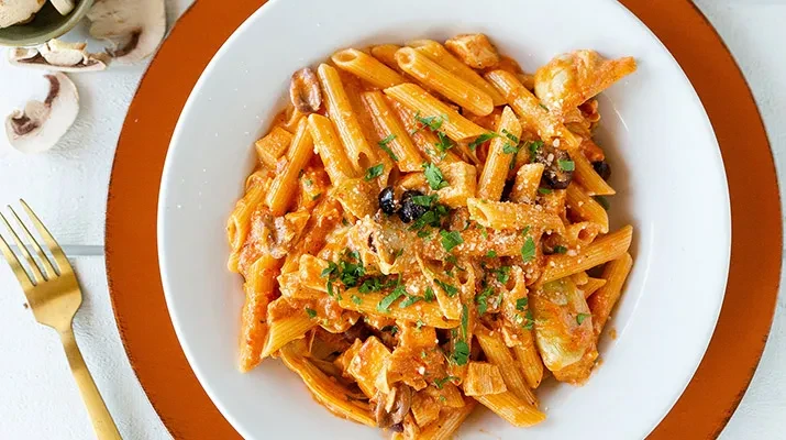 Overhead penne pasta with creamy sauce, cheese, olives, mushrooms, and herbs.