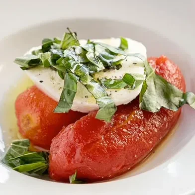 Peeled red tomatoes topped with mozzarella, fresh basil, pepper, and olive oil.