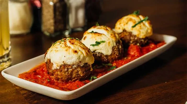 Three large meatballs with melted cheese and herbs on marinara.