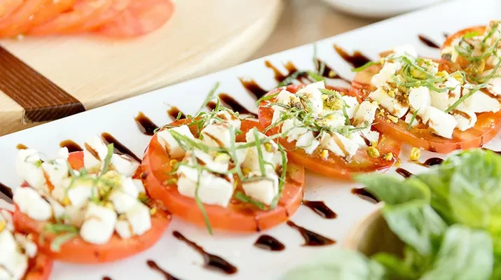 Plated Caprese salad with tomatoes, cheese, basil, pistachios, and balsamic glaze.
