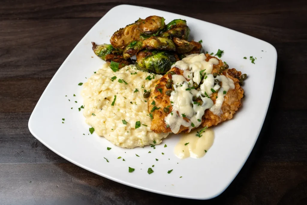 Plated chicken, risotto, and brussels sprouts on a square white dish.