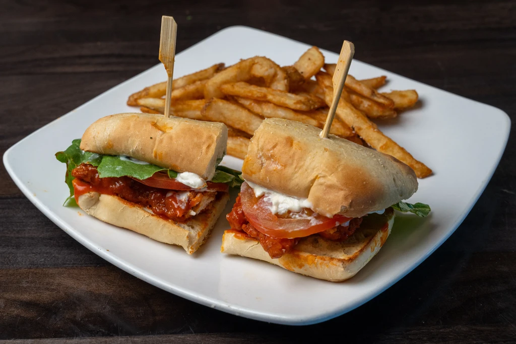 Two saucy sliders, tomato, lettuce, seasoned fries on plate.