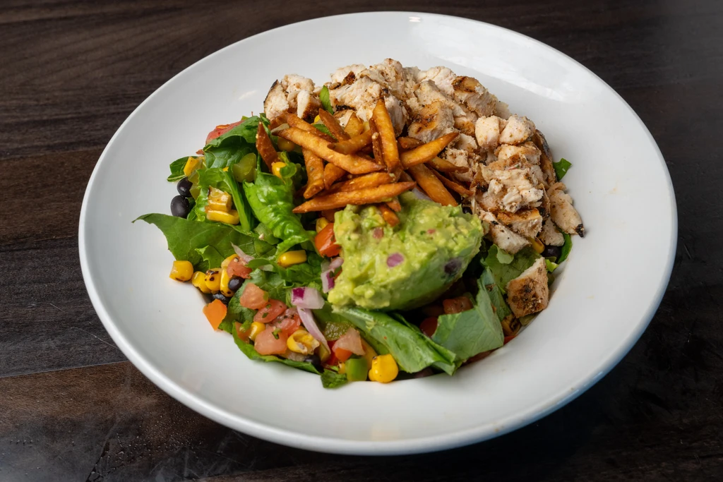 Hearty bowl of grilled chicken, guacamole, green salad, and crispy strips.