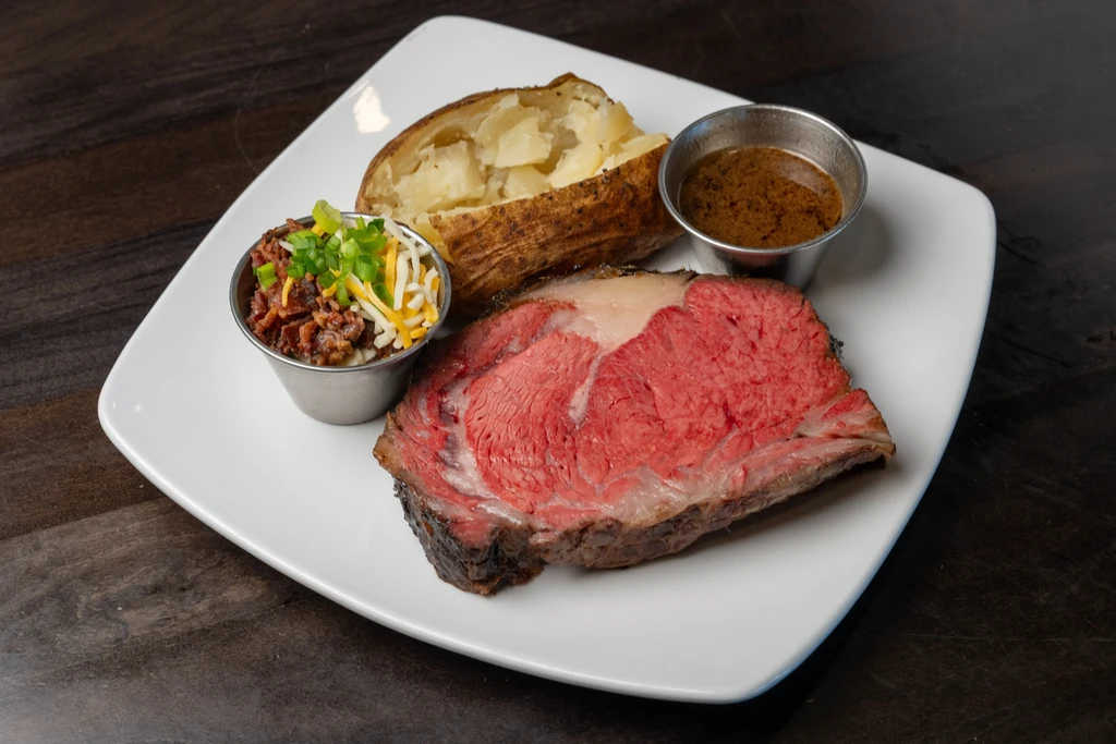 Pink-red prime rib, baked potato, loaded toppings, and au jus.