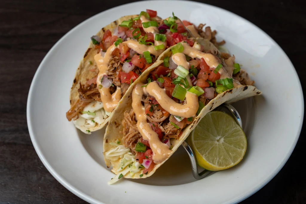 Two soft tacos with shredded meat, pico de gallo, sauce, and lime.