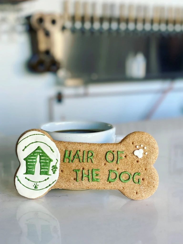 Dog bone cookie decorated with "HAIR OF THE DOG" beside coffee.