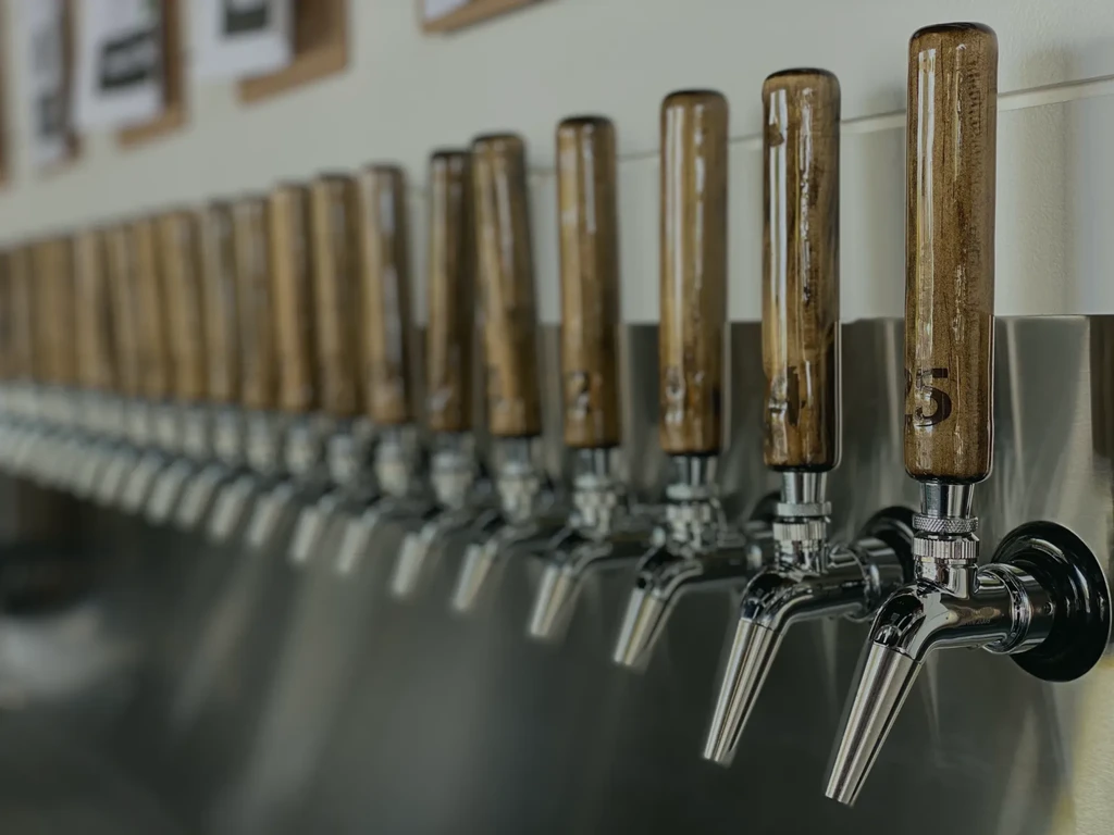 Long row of beer taps, silver spigots and wooden handles.