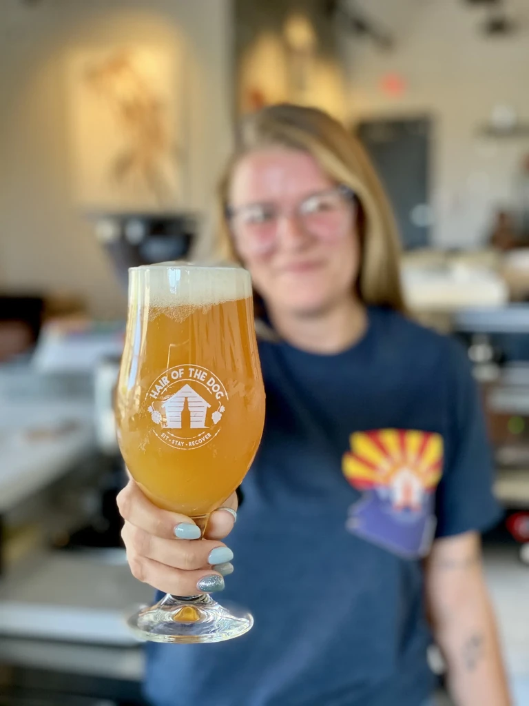 Hand with blue nails holds a stemmed glass of Hair of the Dog beer.