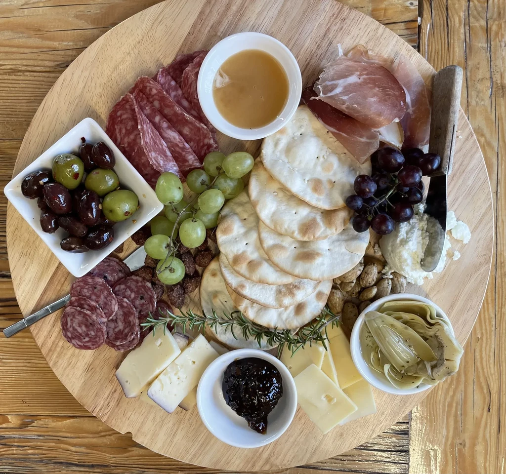 Vibrant wooden charcuterie board with meats, cheeses, fruits, crackers, and olives.