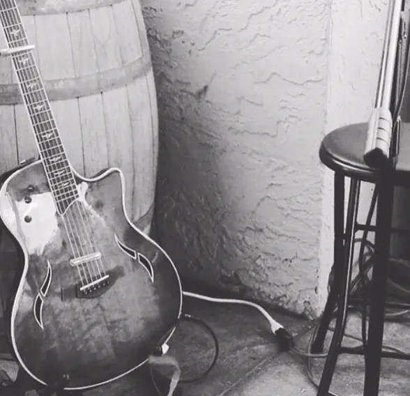 Black and white acoustic-electric guitar, barrel, stool, microphone stand.
