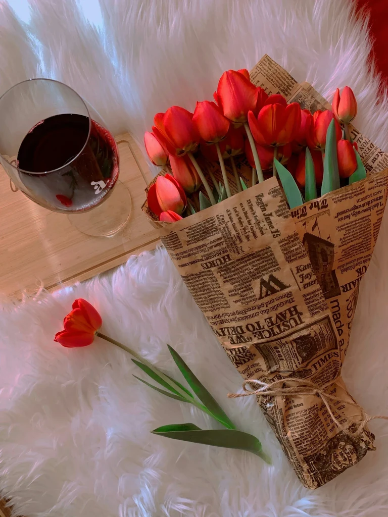 Bouquet and single red tulips, wine glass on white faux fur.