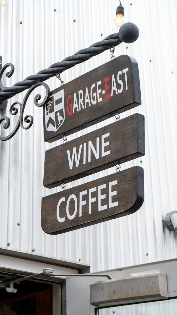 Hanging wooden sign for "GARAGE-EAST WINE COFFEE" on a corrugated wall.