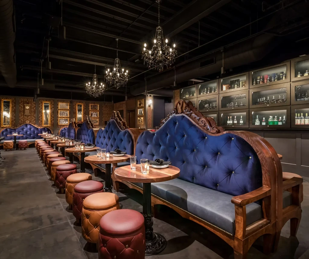 Empty, luxurious bar interior with blue banquettes, tu tufted stools, and chandeliers.