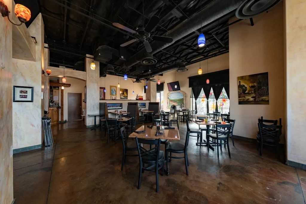 Empty restaurant dining room showing tables, colorful lights, exposed ceiling, and wall art.