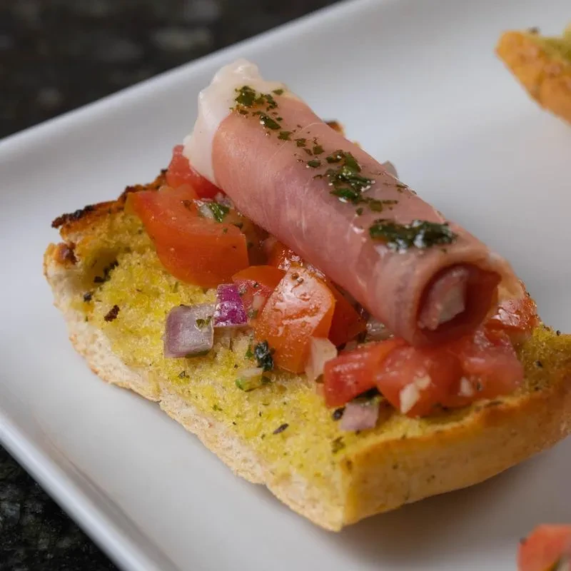 Toasted bruschetta topped with tomato, red onion, prosciutto, and herbs.
