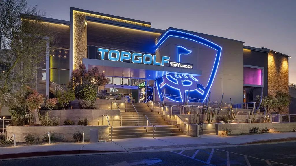 Modern Topgolf exterior at twilight with glowing blue signs and illuminated entrance.