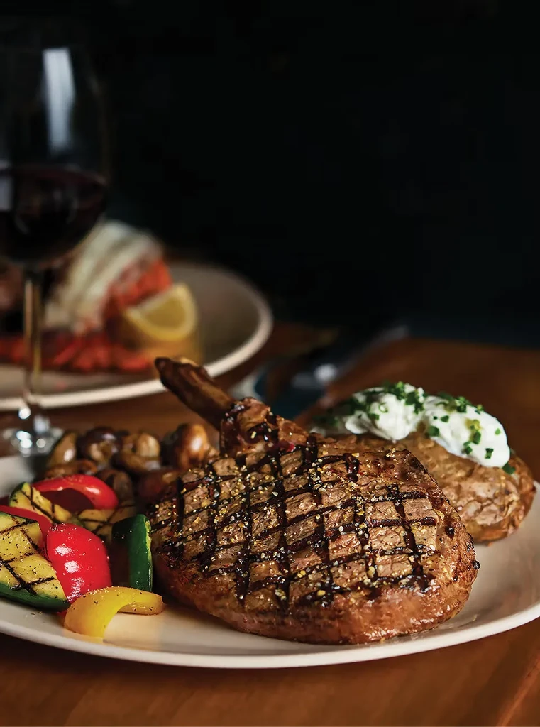Tomahawk steak with grilled vegetables, baked potato, and red wine.