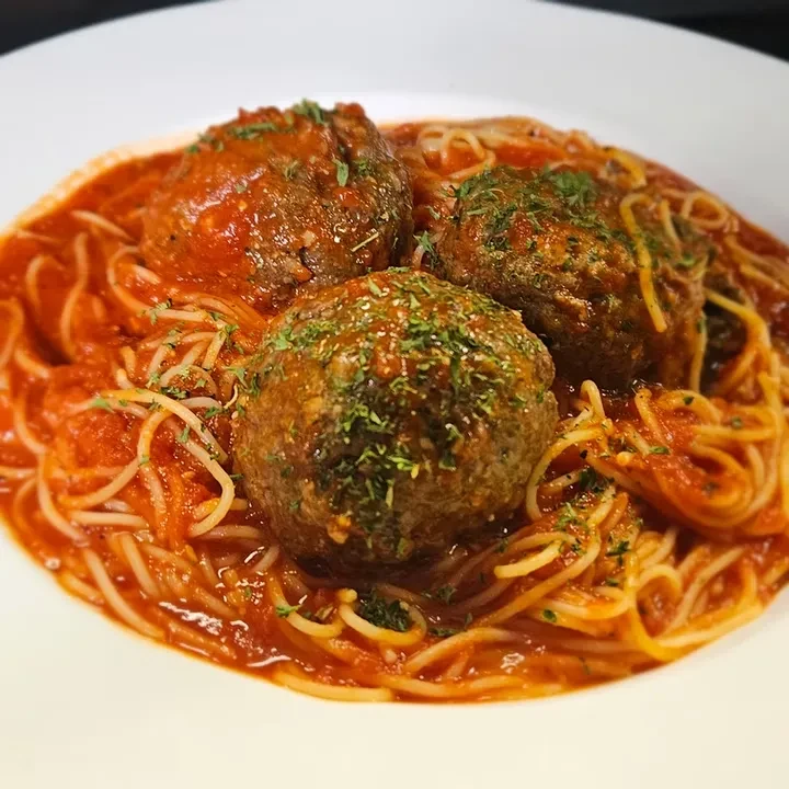 Close-up: spaghetti and three meatballs with red sauce, green herbs.