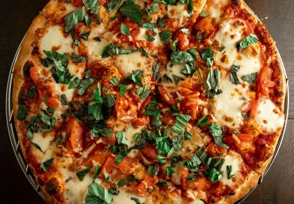 Overhead close-up of a whole pizza with tomato, mozzarella, and basil.