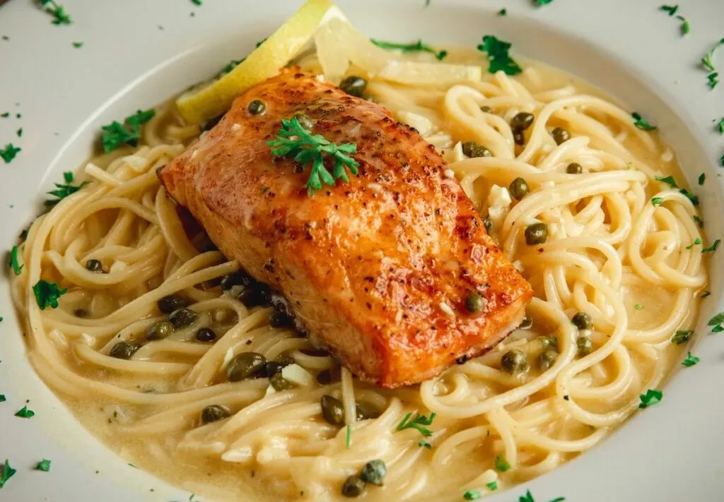 Pan-seared salmon on creamy spaghetti with capers, herbs, and lemon.
