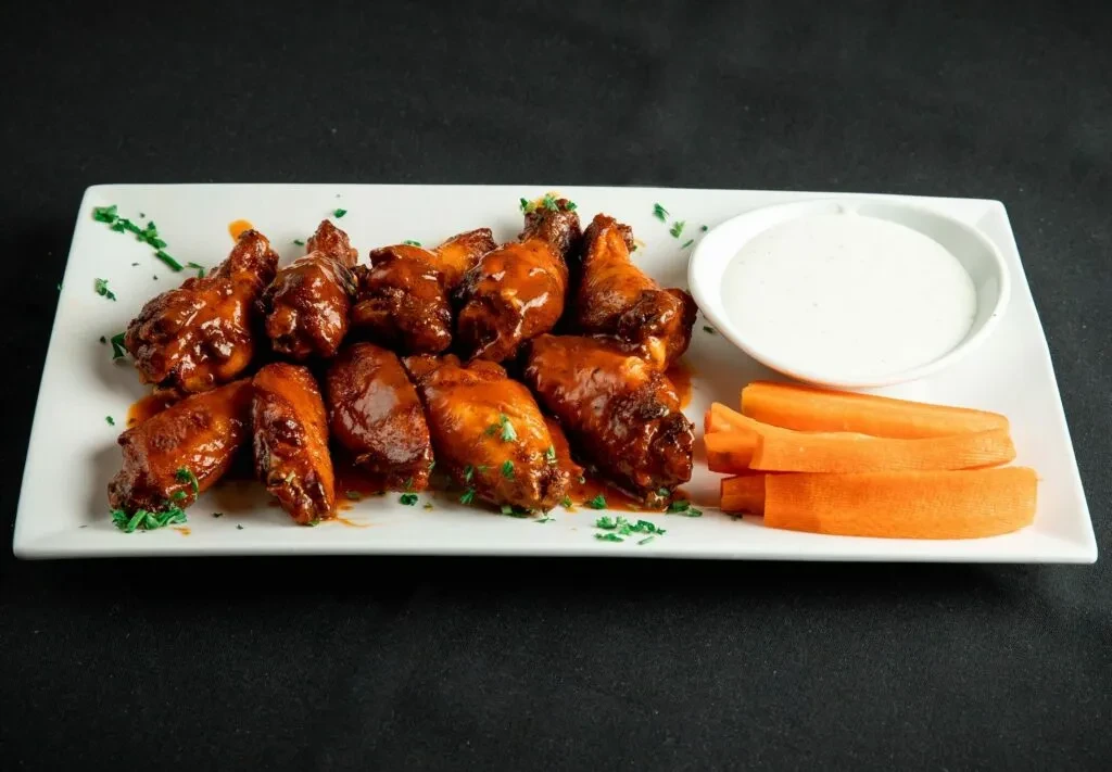 Twelve sauced chicken wings with dip and carrot sticks.