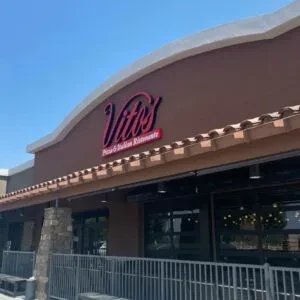 Exterior of Vito's Pizza: brown stucco, red sign, garage-style windows, patio.