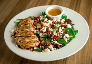 White plate of salad with grilled chicken, cheese, and dressing.