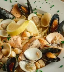 Seafood pasta dish with mussels, clams, salmon, lemon, and green herbs.