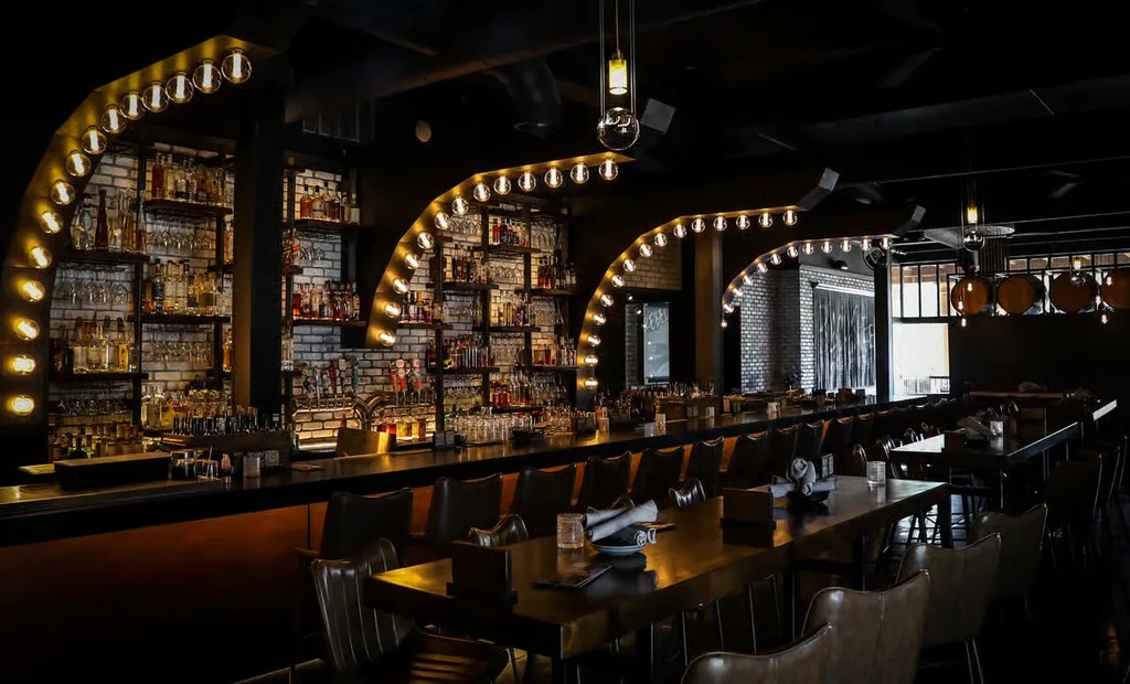 Empty, dimly lit bar with exposed brick, liquor, and warm lights.