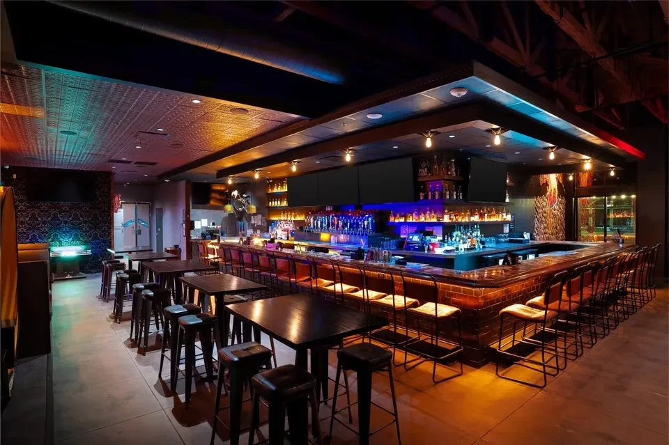 Modern bar with long counter, stools, and vibrant blue-orange lighting.