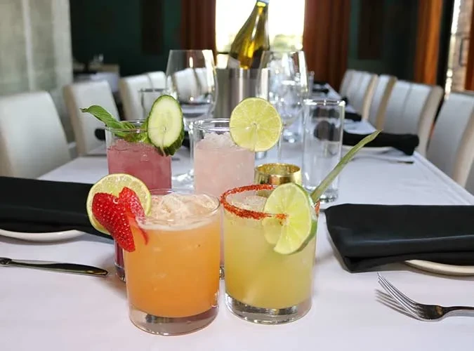 Four colorful, garnished cocktails on an elegant restaurant table.