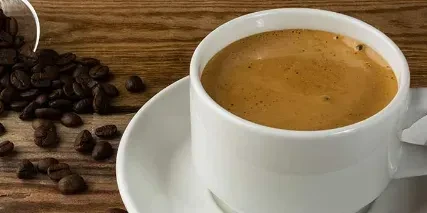 White coffee cup, saucer, and coffee beans on rustic wood.