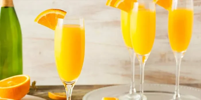 Mimosas in flutes with orange slices, a champagne bottle, and cut orange.