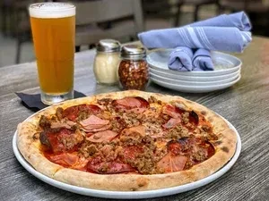Freshly baked meaty pizza, a glass of beer, and table setting.