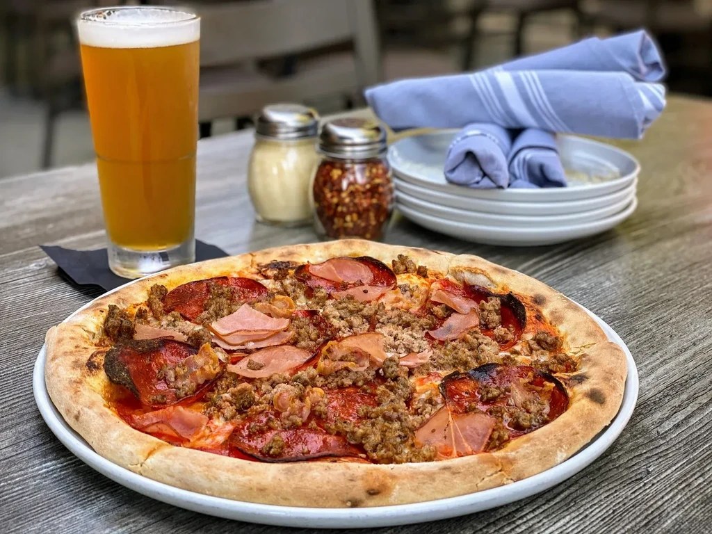 Meat pizza and beer on a wooden restaurant table.