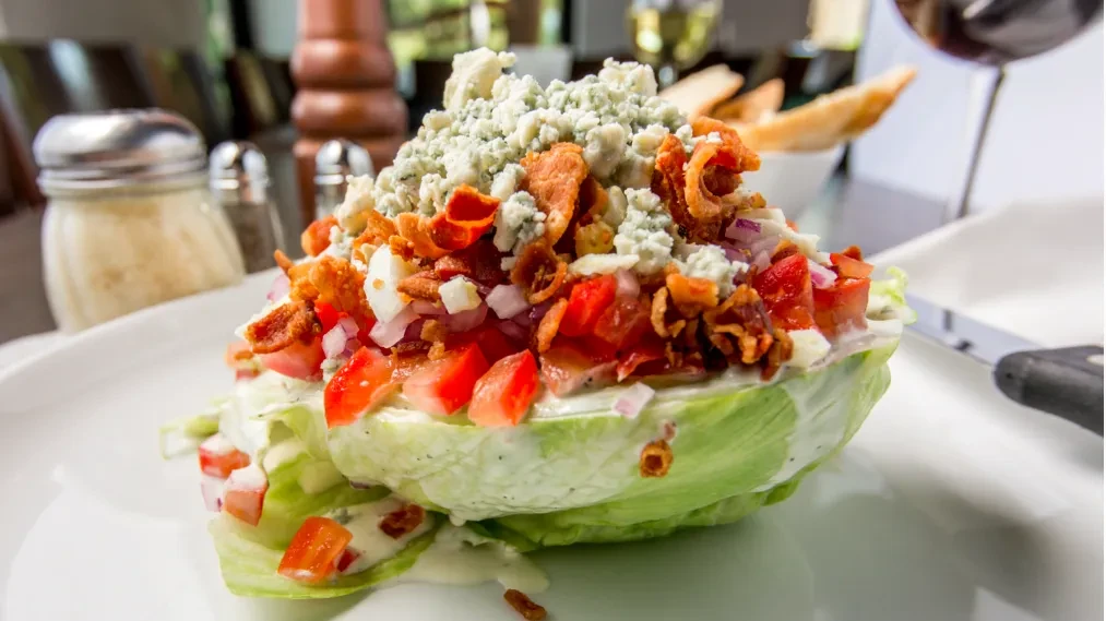 Close-up of a wedge salad with blue cheese, bacon, tomatoes, and onions.