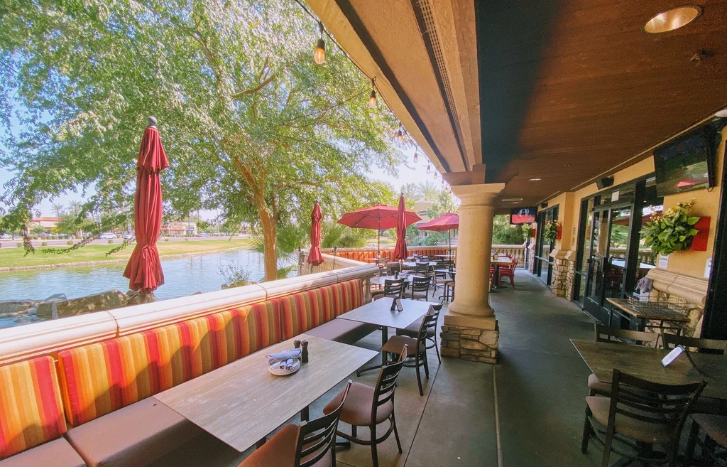 Empty restaurant patio with striped cushions overlooking water.