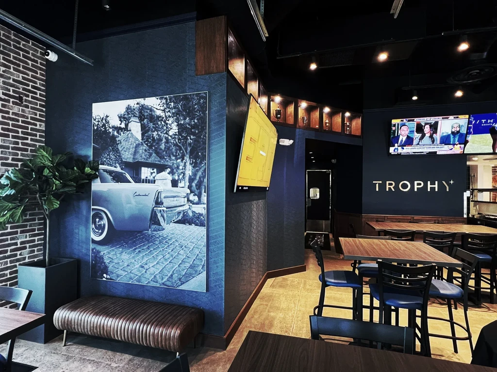 Modern restaurant interior with dark blue walls, vintage car art, and multiple TVs.