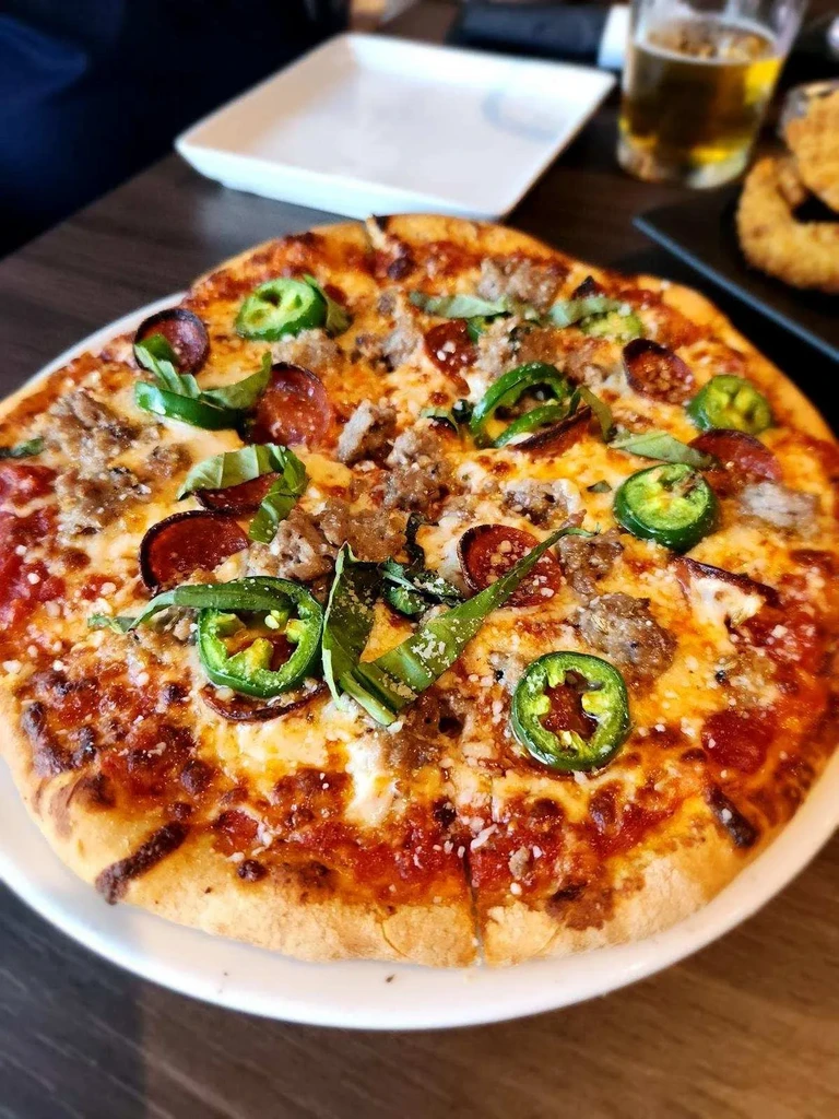 Close-up, top-down pizza with pepperoni, sausage, jalapeños, cheese, and basil.