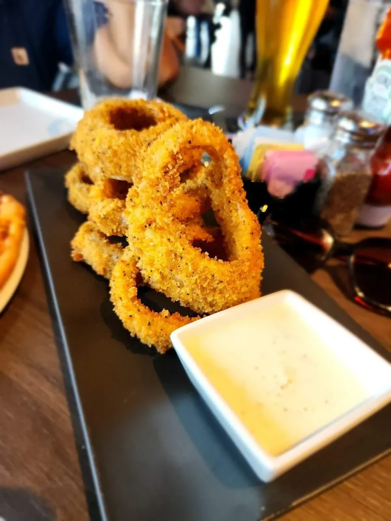 Piled crispy onion rings with dipping sauce on a black plate.