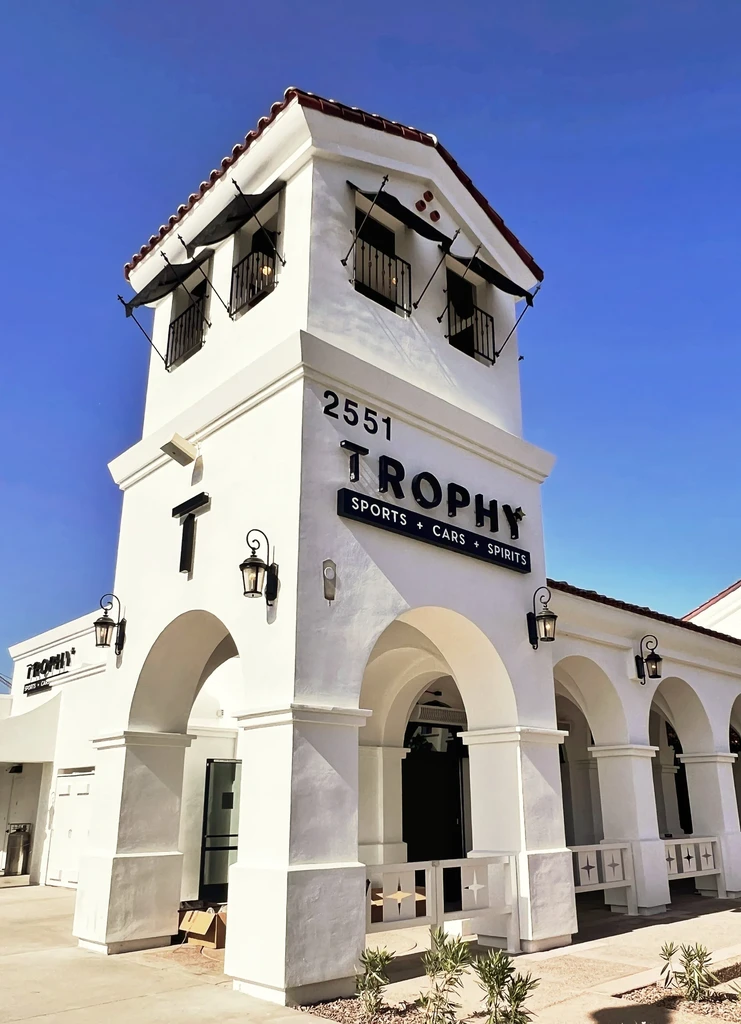 White stucco Spanish colonial building with "TROPHY" sign and red tile roof.