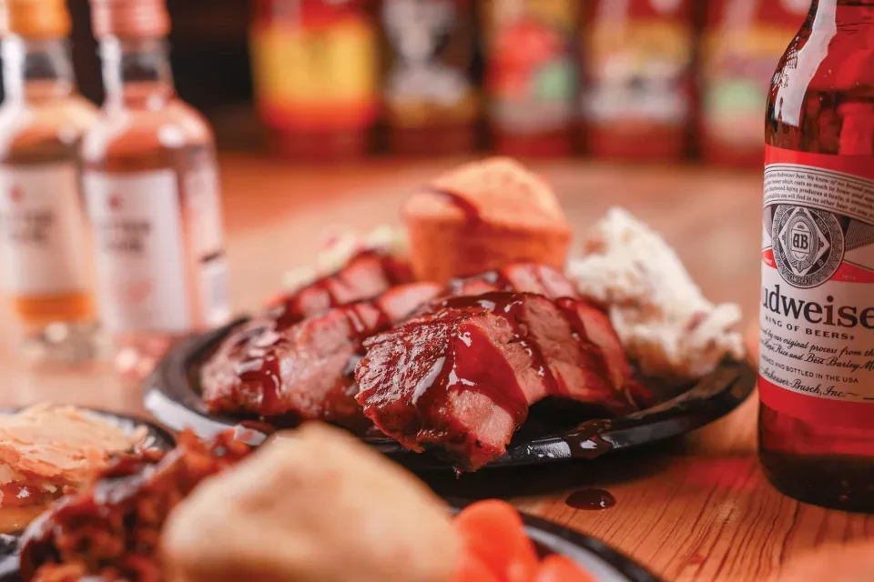 Sliced barbecued meat, cornbread, coleslaw, and Budweiser beer.