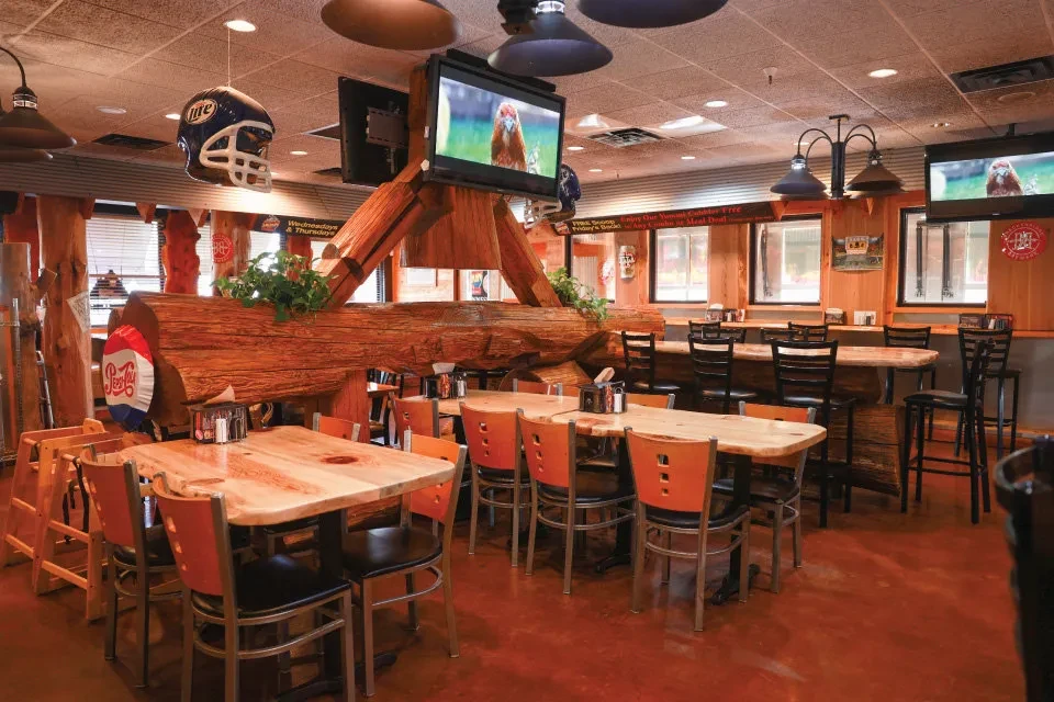 Empty casual restaurant interior with rustic log decor and TVs.