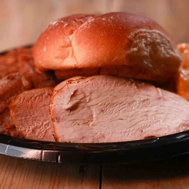 Close-up of sliced cooked meat and bread rolls on a black platter.