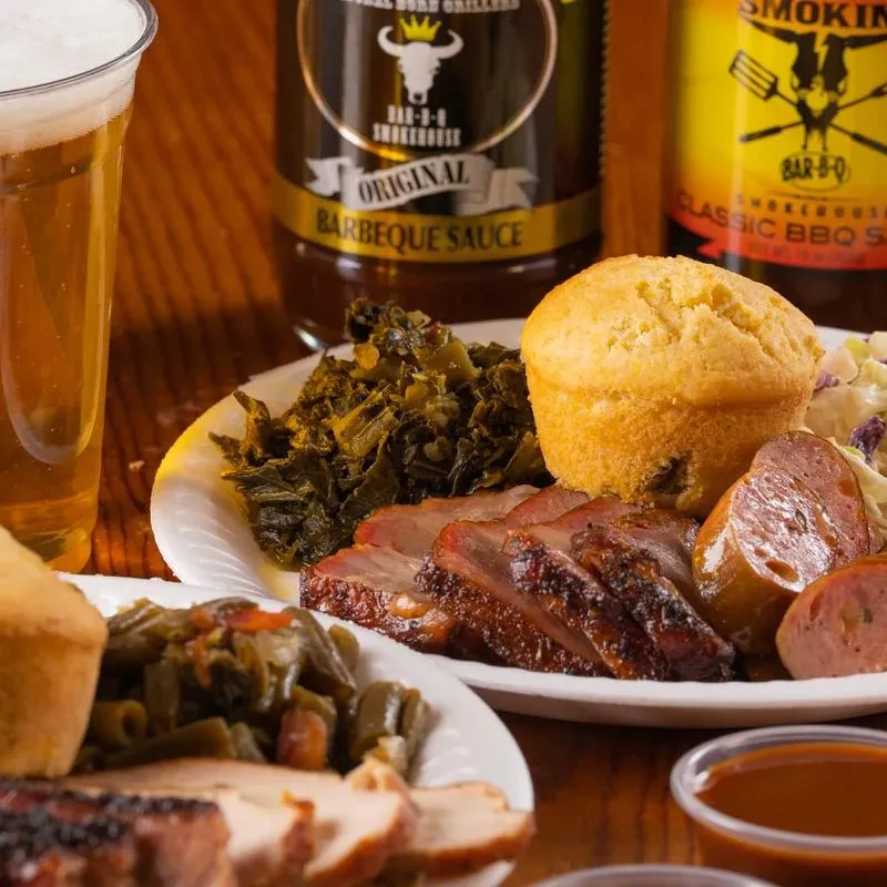 Close-up of rustic table with BBQ meats, sides, drinks, and sauces.