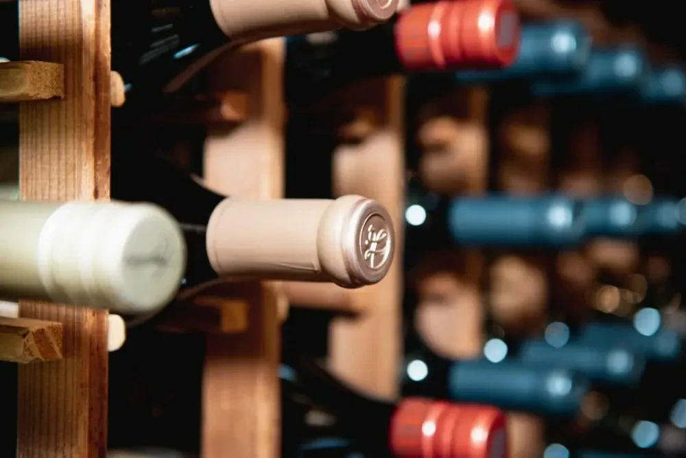 Close-up of wine bottles horizontally in a wooden rack with varied foils.