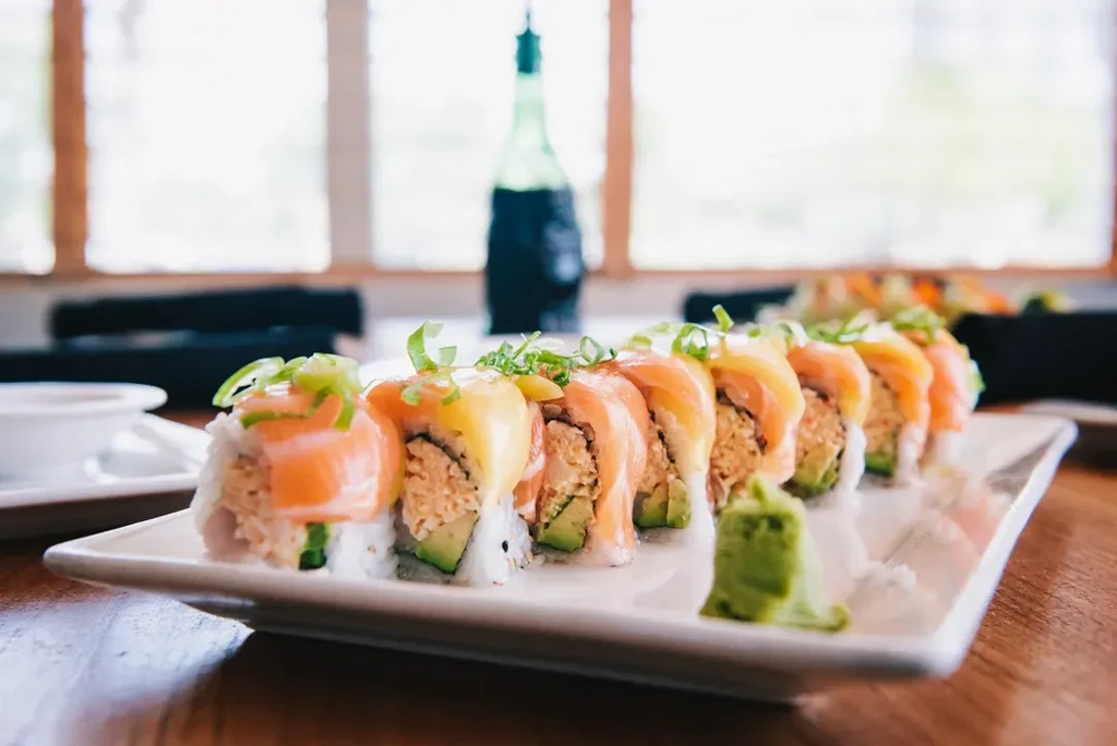 Eleven salmon sushi rolls with green onions and wasabi.